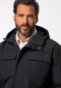 Laivasto sininen huppujacketti, joka on valmistettu kestävästä kankaasta ja jossa on neljä etutaskua, nepparit ja vetskari edessä. Teksturoitu materiaali ja säädettävät elementit.