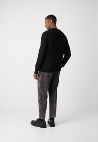 Jersey negro de punto con cuello redondo, combinado con pantalones gris rayados y zapatos negros de cordones, mostrando un ajuste relajado y una tela texturizada.