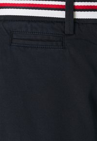 Tejido azul marino con una textura sutil que cuenta con un pequeño bolsillo horizontal y una banda a rayas en rojo, blanco y negro.