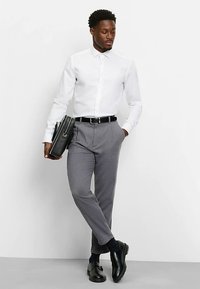 Weißes Hemd mit Knöpfen, graue maßgeschneiderte Hose, schwarze Lederschuhe, schwarzer Gürtel und eine schwarze Tasche. Schlichtes Design mit klassischer Passform.