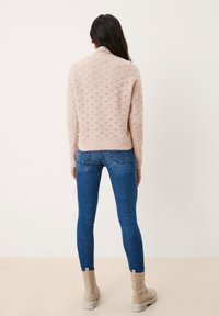 Pull rose clair en maille avec un motif en losange texturé, associé à un jean skinny bleu et des bottines beige, vu de dos.