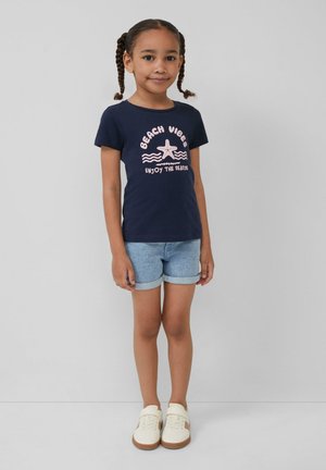 Granatowy bawełniany t-shirt z grafiką "BEACH VIBES", rozgwiazdą i falami; w zestawieniu z jasnoniebieskimi szortami dżinsowymi; białe trampki.