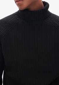 Suéter de cuello alto de punto acanalado negro con diseño de manga raglán, que presenta un patrón texturizado. Tela suave y lisa.