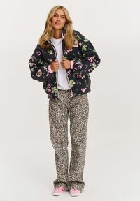 Čierna pufová bunda s kvetinovým vzorom a ružovými akcentmi, skombinovaná s béžovými nohavicami s leopardím vzorom a ružovými teniskami. Oblečenie má uvoľnený strih.