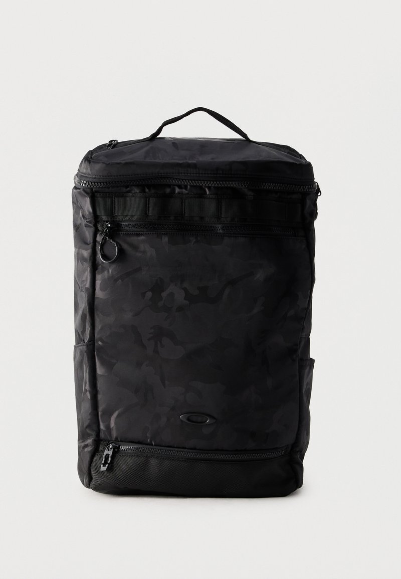 Μαύρο ορθογώνιο σακίδιο με διακριτικό καμουφλάζ, επάνω χερούλι, πολλαπλές θήκες με φερμουάρ και μικρό οβάλ λογότυπο μπροστά.