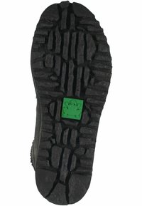 Suela de zapato negra con un patrón de agarre robusto y un acento de rana verde. La textura es áspera con surcos profundos para tracción.