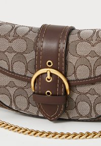 Brown patterned fabric handbag with dark brown leather strap and gold buckle, featuring a gold chain handle on a white surface.