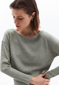 Ljusgrå, långärmad ribbad tröja med vid halsringning och strukturerad tyg. Ärmarna har en figurnära passform som framhäver silhuetten.