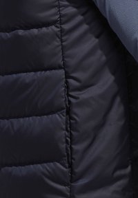 Gros plan d’un tissu matelassé noir avec des coutures horizontales à côté d’un tissu bleu foncé texturé.
