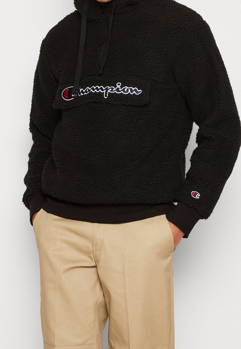 Schwarzer Fleece-Hoodie mit Kängurutasche, gesticktem "Champion"-Logo auf der Vorderseite, verstellbarem Kordelzug an der Kapuze und gerippten Bündchen.