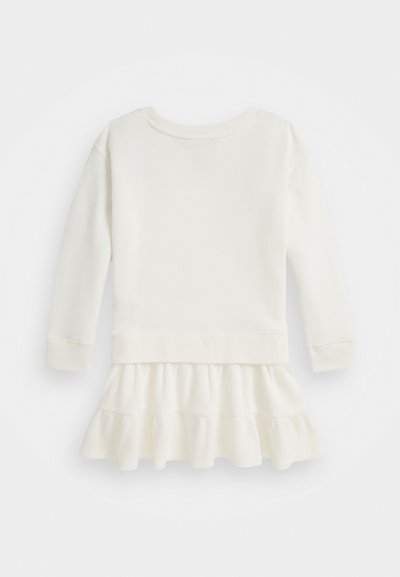 Ilgi piedurkņu, krēmkrāsas kleita ar ribotu tekstūru un izplestu ziedlapu apakšmalā, kurai ir vienkāršs apaļais kakls un aproces piedurknes.