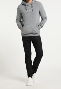 Sweat à capuche gris avec poche kangourou, capuche à cordon de serrage et détail brodé. Associé à un pantalon noir et des baskets blanches.