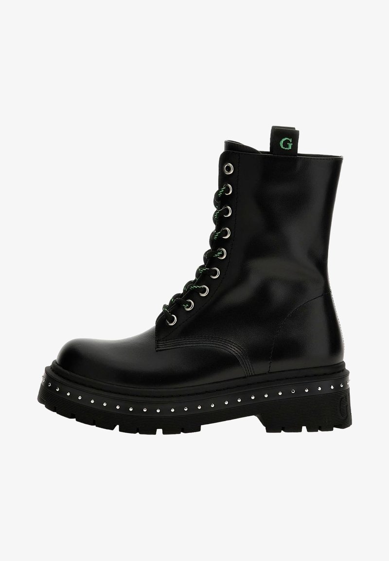 Botas de cuero negras hasta el tobillo con cordones verdes, ojales plateados y plataforma con tachuelas. Incluyen una lengüeta de tira y suela texturizada.