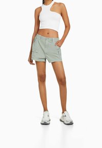 Gröna cargoshorts med dubbla sidofickor, i kombination med en vit ribbad croptop. Modellen bär grå och vita sneakers.