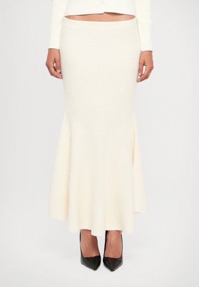 Witte, getextureerde, aansluitende zeemeerminrok met een uitlopende zoom. Zwarte puntige hakken accentueren de look. Geschikt voor formele of semi-formele gelegenheden.