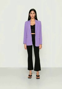 Blazer lilás com lapelas em bico, top cropped de renda preto e calças flare pretas de cintura alta, complementados por sandálias pretas de salto.