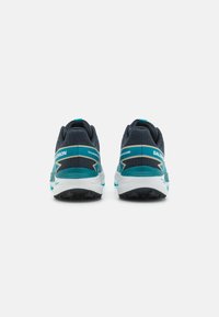 Scarpe da trail running con una tomaia blu scuro e accenti turchesi, un tallone testurizzato e una intersuola bianca; suola nera robusta per una buona aderenza.