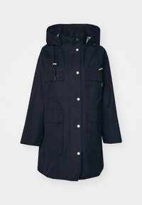 Námořnická voděodolná parka s kapucí, zdobená zlatými kovovými detaily, více předními kapsami a uvolněným střihem. Hladká textura, pohodlný design.