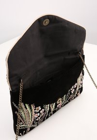 Bolso de terciopelo negro con bordado floral en rosa y verde, que cuenta con un cierre de botón dorado y una correa de cadena para el hombro.