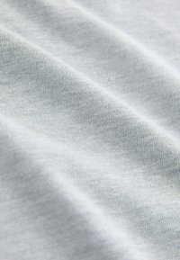 Primo piano di tessuto grigio chiaro con pieghe morbide e motivo a maglia visibile.