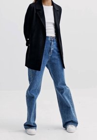 Black long blazer, white fitted t-shirt, loose blue jeans, and white sneakers. Smooth fabric; classic collar and button accents on sleeves.