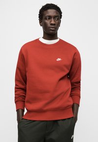Sweatshirt vermelho de algodão com mangas compridas, punhos canelados e gola redonda. Apresenta um pequeno logótipo branco da Nike no peito.