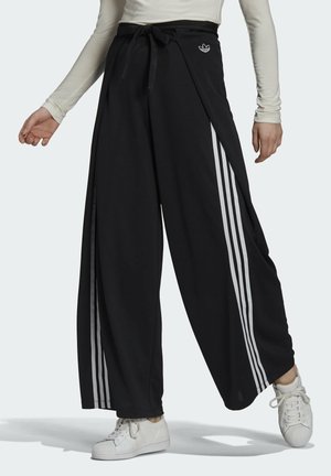 Pantalons larges noirs avec une taille à nouer, présentant trois bandes verticales blanches de chaque côté et un logo brodé sur le devant.