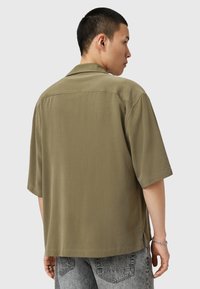 Korte mouwen, olijfgroen shirt van zachte stof met een losse pasvorm, voorzien van een kraag en zijsplitten aan de onderrand voor mobiliteit.