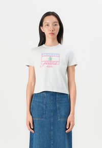 Šedé skrátené tričko s krátkymi rukávmi, s multicolor textom "tommy jeans" a logom. Skombinované s modrou džínovou sukňou.