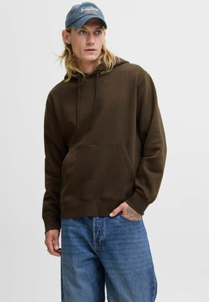 Brown hoodie with a front pocket and drawstring. Paired with light blue jeans. A blue cap is worn, featuring text on the front.