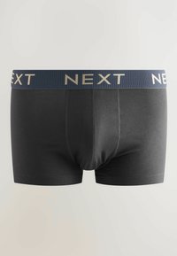 Svarta herrboxershorts med en marinblå midjeresår som har ordet "NEXT" i beige, visade på en ljus, enkel bakgrund.