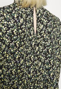Robe noire à fleurs avec un motif vibrant de fleurs jaunes et vertes, détail en forme de clé au dos et tissu texturé.