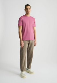 Rosa Rundhals-T-Shirt mit kurzen Ärmeln, kombiniert mit hellbraunen, gestreiften Hosen. Getragen mit weißen Sneakers mit grünen Akzenten.