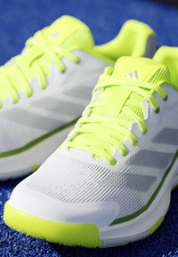 Pair of white and neon yellow running shoes with laces, placed on a blue textured surface.