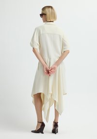 Vestido de crema claro con un dobladillo asimétrico, mangas cortas y tejido suave; combinado con cuñas de color burdeos oscuro.