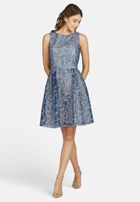 Spitzenkleid in Blautönen, mit tailliertem Oberteil, ausgestelltem Rock und gebundenem Taillengürtel. Leichte Textur mit Blumendesign.
