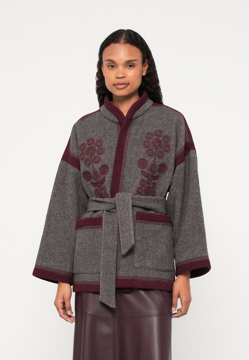 Γκρι μπουφάν από μείγμα μαλλιού με μπορντό λεπτο�μέρειες. Διαθέτει λουλουδάτη κεντητική, φαρδιά μανίκια και ζώνη στη μέση. Υφή υφάσματος και δύο τσέπες.