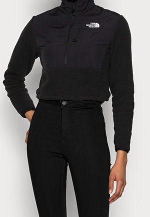 Sudadera de pico negra con cremallera, hecha de suave forro polar con tejido liso en contraste en el pecho; cuenta con un bolsillo con cremallera y un logo en la parte delantera.