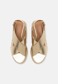 Kullatut espadrille-sandaalit ristikkäisillä nauhoilla, joissa on metallinhohtoinen pinta ja punottu jute-pohja. Littee muoto, avoin varvas ja säädettävä solki.