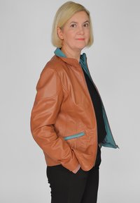 Brun läderjacka med en turkos innervik, med dragkedja fram och sidofickor. Designen inkluderar en ståkrage och en figursydd silhuett.