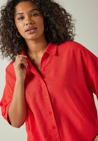 Camisa roja abotonada hecha de tejido ligero, con un corte relajado, mangas cortas y una superficie de textura suave.