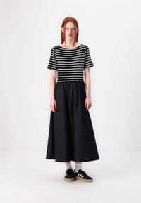 Stribet svart og hvit kortermet topp med svart maxiskjørt. Modellen har på seg svarte sneakers med en beige såle og grå sokker. Glatt tekstur.
