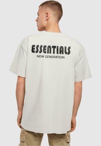 Camiseta de algodón blanca con texto en negrita y apilado en la parte posterior, que dice "ESENCIALES NUEVA GENERACIÓN". Corte relajado y mangas cortas.