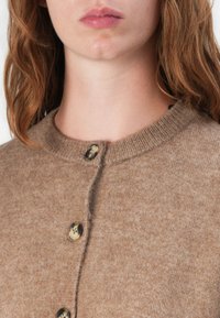 Brun strikket cardigan med rund hals, ribbet struktur og tre store knapper foran, som viser et mykt og komfortabelt materiale.