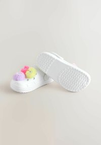 Biele nazúvacie dreváky s tromi farebnými fuzzy pom-pommi: ružová, fialová a žltá. Štruktúrovaná podrážka s vzorovaným gripom.
