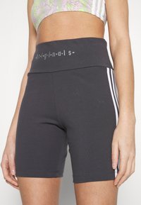 Svarte idrettsshorts med høy midje, med hvite tre-stripe detaljer på sidene og en gråtrykt logo på midjen.