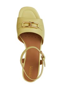 Sandal in pelle gialla con punta quadrata, caratterizzata da una fibbia in metallo dorato e una soletta marrone. Design a fasce con cinturino alla caviglia regolabile.