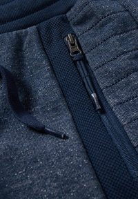 Joggers bleu marine avec fermeture éclair, taille texturée, cordon de serrage et panneaux tricotés contrastants. Détails en tissu légèrement moucheté partout.