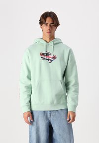 Světlezelená mikina s kapucí vyrobená z měkké tkaniny, na přední straně s grafickým motivem auta a červeným textem podél rukávu. Obsahuje klokaní kapsu.