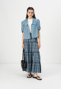 Denim jasje met pofmouwen, getailleerd ontwerp, lichtblauwe kleur. Geruite tiered rok, blauw-wit patroon, zwarte tas en zwarte slippers.